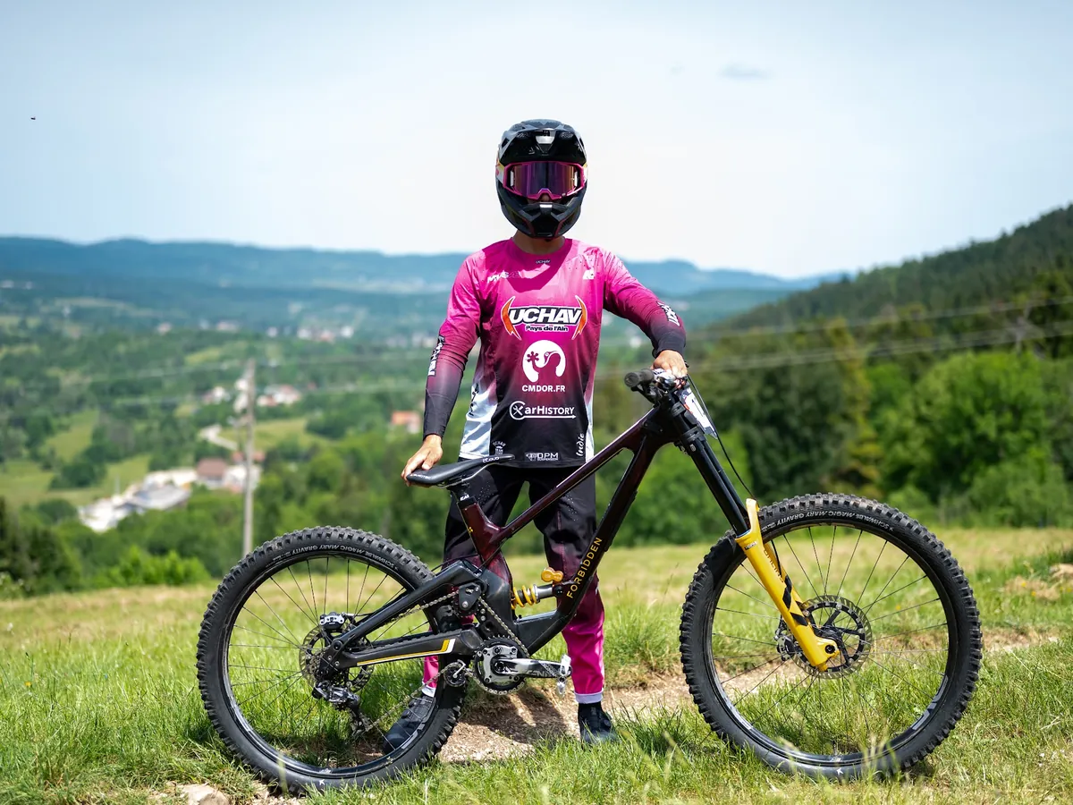 Victor Michaud debout à côté de son vélo de descente, face à la vallée